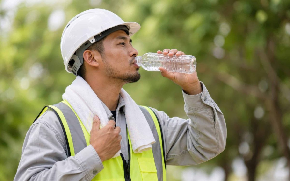 Construction worker drinking water outdoors in hot weather.