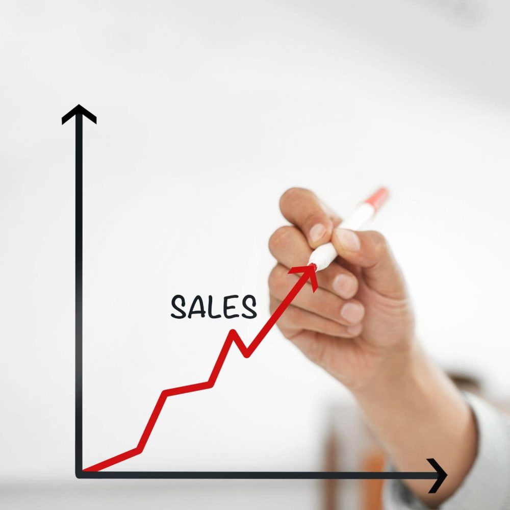 Hand drawing an upward sales trend line on a graph for online training.