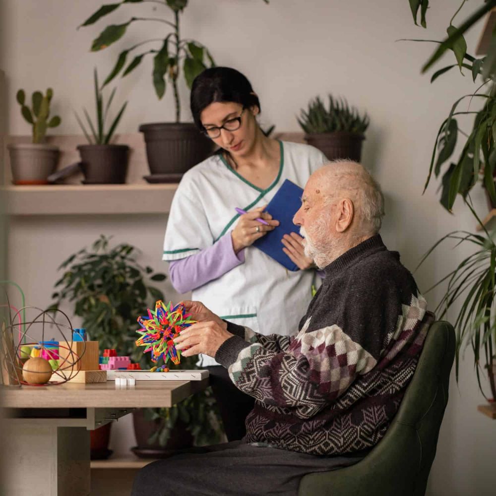 Elderly man engaging in a craft activity with caregiver in a care setting.