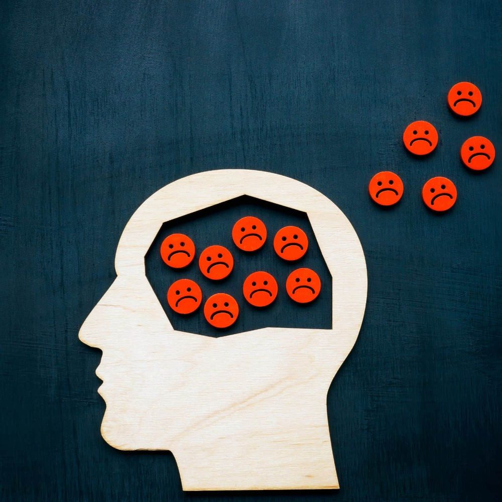 Silhouette of a human head with sad face icons inside and outside.