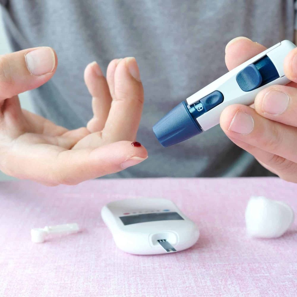 Person testing blood sugar with a glucometer and lancet device.