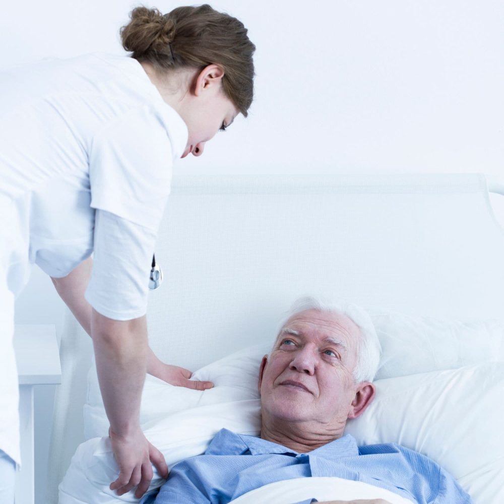 Nurse providing care to elderly man in hospital bed.
