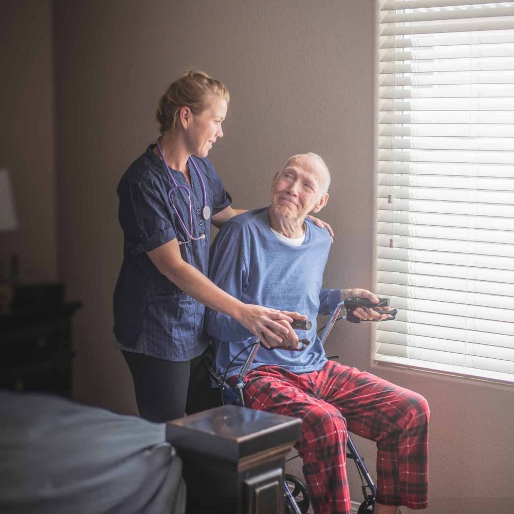 Care worker helping elderly man in a wheelchair at home.