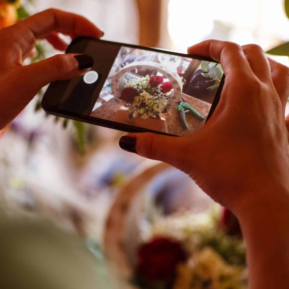 Person capturing floral arrangement with smartphone for social media.