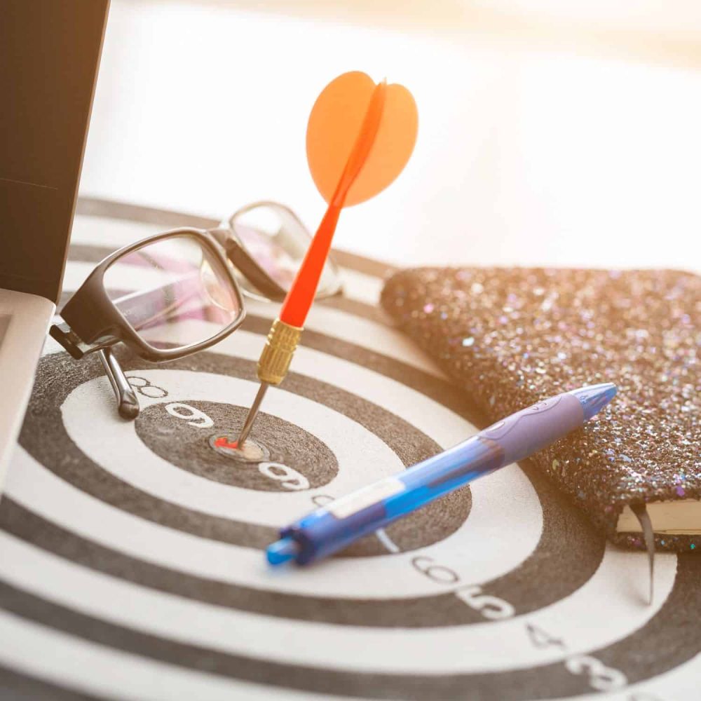 Dart hitting the bullseye on a target with a pen and notebook nearby.
