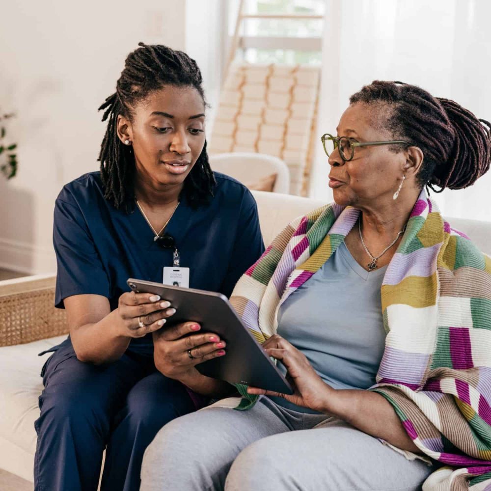 Care worker assisting an elderly woman with online training on a tablet.