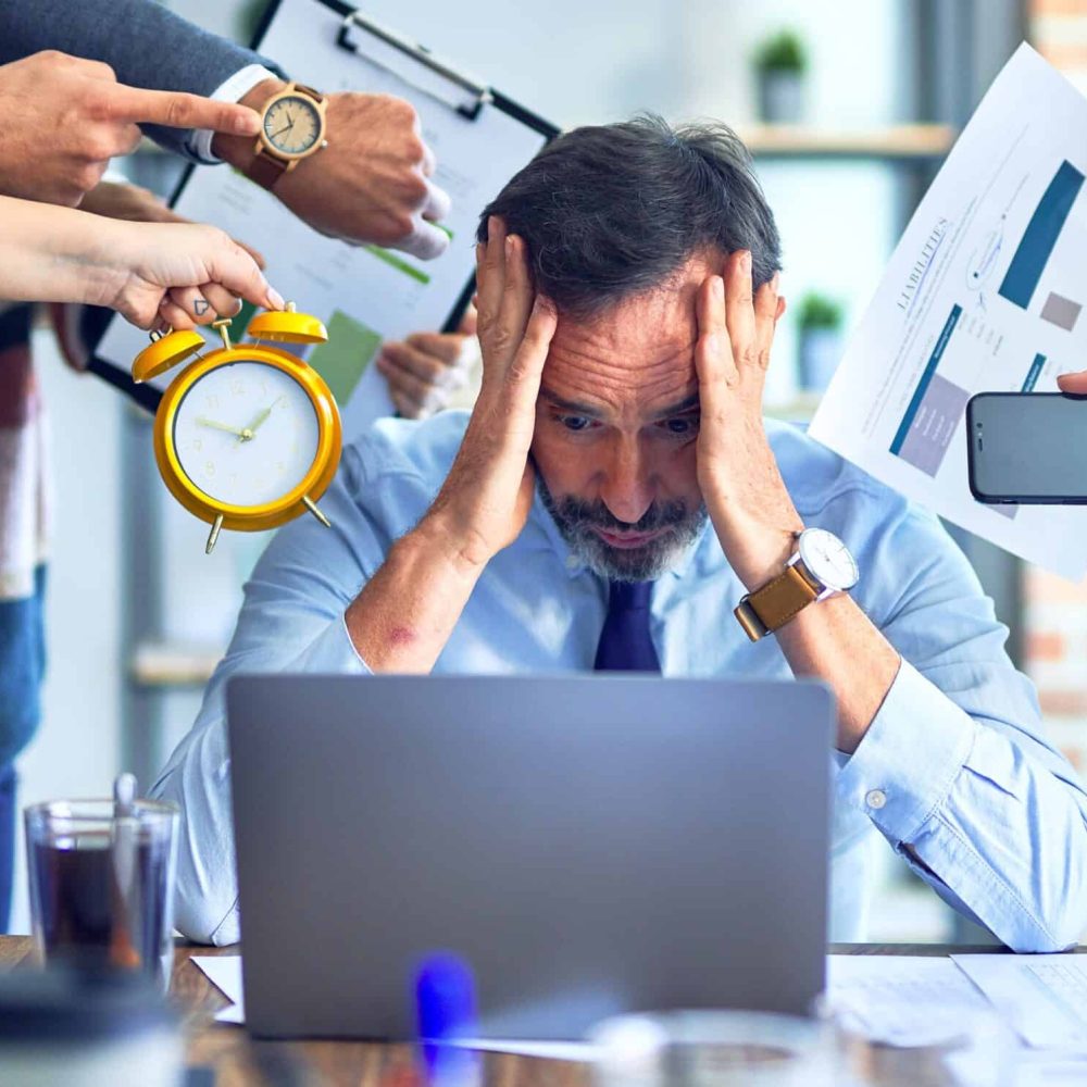 Overwhelmed man at work surrounded by colleagues with clocks and charts.