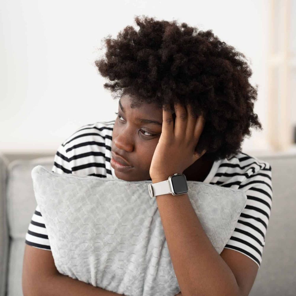 Young woman feeling distressed, holding pillow, representing mental health awareness.