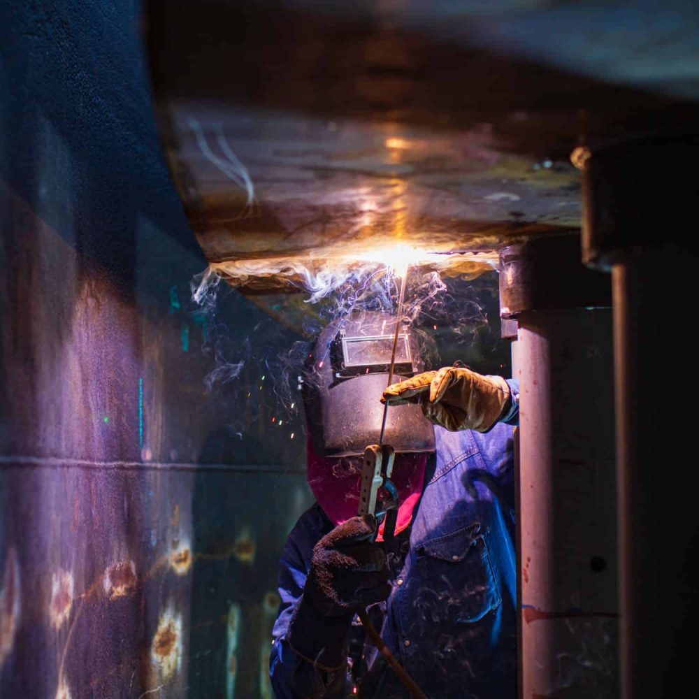 Worker welding inside a confined space with protective gear and sparks flying.