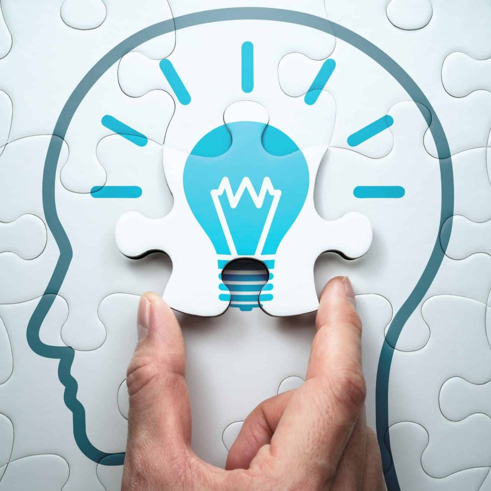 Hand placing lightbulb puzzle piece in brain outline for problem solving.